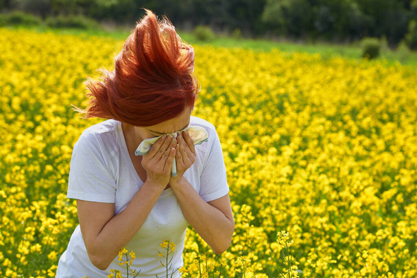 Allergisch gegen Pollen und Blütezeit: Ein Mädchen niest in einem Blumenfeld - Foto, Bild