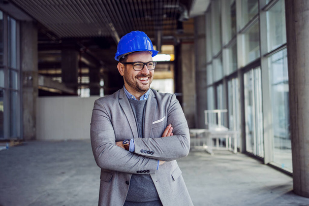 Portrét pohledného úspěšného architekta stojícího se zkříženýma rukama ve stavebnictví. - Fotografie, Obrázek