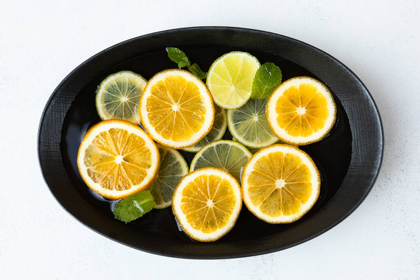 fresh and juicy sliced lemon and lime slices in water, in a black bowl on a white background, citrus background. beauty and health concept. - Foto, Bild