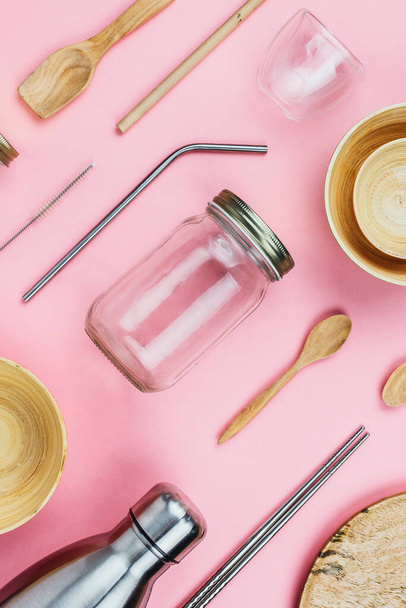 Flatlay of various sustainable zero waste kitchenware utensils and dishware: glass and metal bottles, wooden bamboo bowls, eco straws etc on pink - Foto, afbeelding