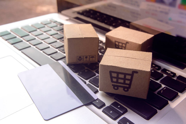 Online nakupování - Papírové krabice nebo balíček s logem nákupního košíku a kreditní kartou na klávesnici notebooku. Nákupní servis na webu a nabízí doručení domů - Fotografie, Obrázek