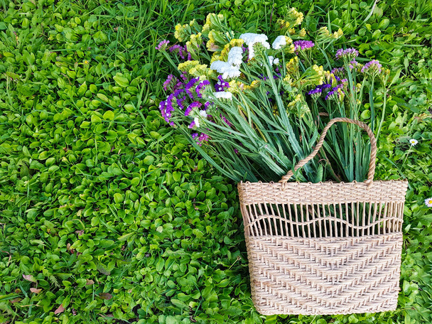 Вид соломенной дамской сумки с цветами на фоне травы
. - Фото, изображение