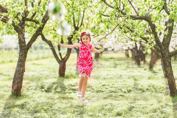 boldog lány piros ruhában fut egy virágzó kertben. - Fotó, kép