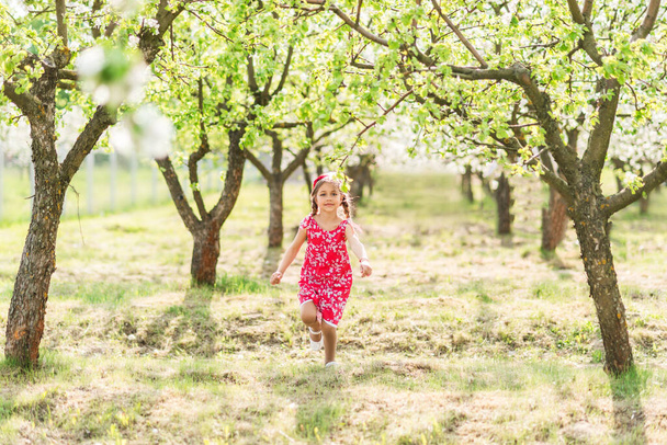 felice ragazza in un sundress rosso corre in un giardino fiorito
. - Foto, immagini
