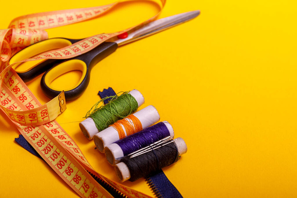 Vlakke lay van gekleurde draad rollen en schaar voor het naaien van gele achtergrond. Naai-en handwerk concept. Gereedschap voor naaien en handmaken: draad, schaar. - Foto, afbeelding