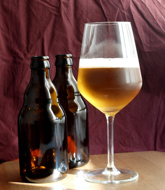 dvě hnědé skleněné láhve od piva a jednu sklenici čerstvého piva přes tmavou tkaninu na pozadí       - Fotografie, Obrázek