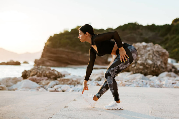 sexy atletische vrouw stretching oefeningen workout outdoor. Sportieve aantrekkelijke vrouw die traint en zich uitstrekt op het strand bij zonsondergang. Vrouwelijke fitness model jogger in sportkleding. Gezonde levensstijl motivatie. - Foto, afbeelding