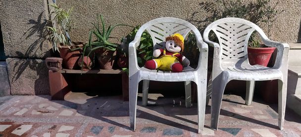 Чучело куклы сидит на пластиковом стуле в одиночестве на заднем дворе в Индии в течение лета в блокировке коронный вирусный период 2020
 - Фото, изображение