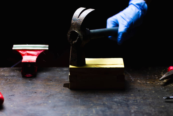 mano con guantes azules golpeando con caja de madera martillo, concepto de reparación, mantenimiento y artesanía en un fondo negro
. - Foto, imagen