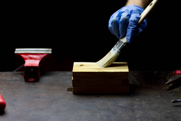 verniciatura a mano scatola di legno artigianale con guanti blu su sfondo nero, concetto di riparazione e manutenzione di artigianato
. - Foto, immagini