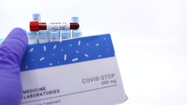 Arzt zeigt Medikamentenbox für Covid-19 Behandlung. Konzept der Covid Stop Medizin mit Blutteströhrchen auf dem Hintergrund. Heilung für Coronavirus, COVID-19 Behandlung. Weiß mit Kopierplatz - Filmmaterial, Video