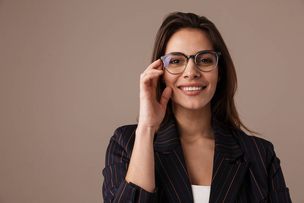 Photo of charming businesswoman in eyeglasses smiling and looking at camera isolated over grey background - Foto, Bild