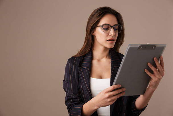 Photo of focused businesswoman in eyeglasses posing with clipboard isolated over grey background - Foto, immagini
