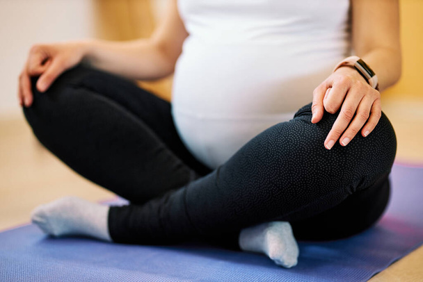 Closeup of pregnant woman sitting in lotus yoga pose and meditating. - 写真・画像