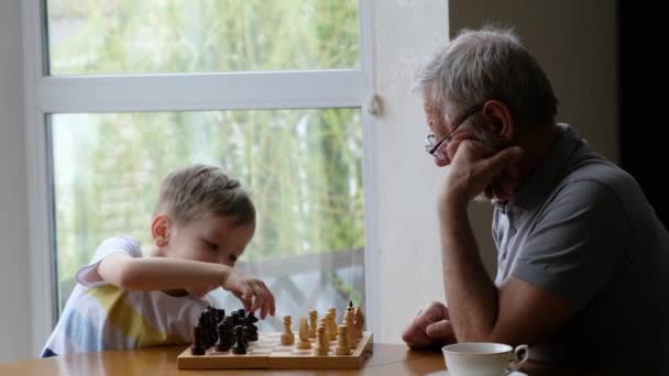 Little boy child play chess with his grandfather, senior positive man - Séquence, vidéo