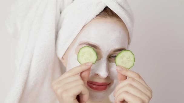 Clean healthy skin care concept. Cheerful happy young woman with hair wrapped in towel, covering eyes with fresh cucumbers, laughing and looking at camera. Close up portrait - Imágenes, Vídeo