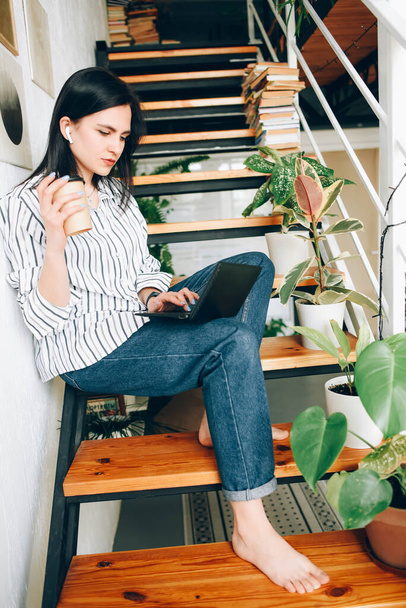 Una ragazza si siede sui gradini con il caffè e lavora in un computer portatile
. - Foto, immagini