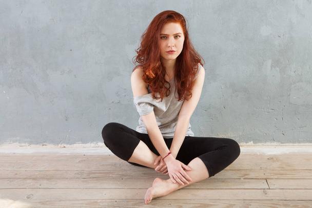 Serious girl's portrait with red hair against the background of a concrete wall - Φωτογραφία, εικόνα