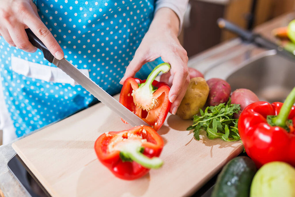 Close up of woman cutting red paprika pepper on cutting board in the kitchen. - Fotó, kép