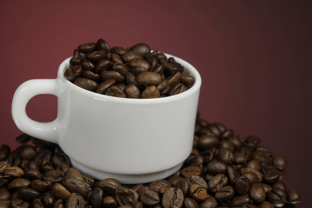 Λευκή κούπα με κόκκους καφέ πασπαλισμένη με κόκκους καφέ σε κόκκινο φόντο - Φωτογραφία, εικόνα