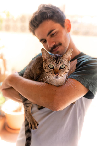 foto vertical. O jovem abraça um gato de olhos verdes. O gato olha para a câmera
. - Foto, Imagem