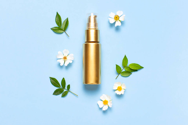 Cosmetic mock up gold bottles. Cosmetics, spring white flowers green leaves on blue background. Cosmetics springtime summer Concept. Flat lay top view copy space. Branding products, beauty background. - Photo, Image