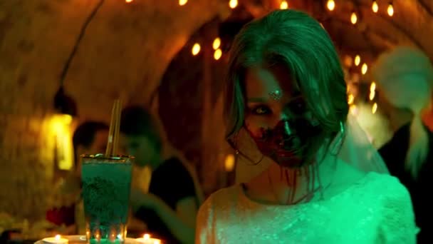 Młoda kobieta ze strasznym makijażem trzyma drinka i świece. Materiał filmowy. Kelnerka z przerażającą twarzą zombie podczas Halloween w klubie nocnym. - Materiał filmowy, wideo