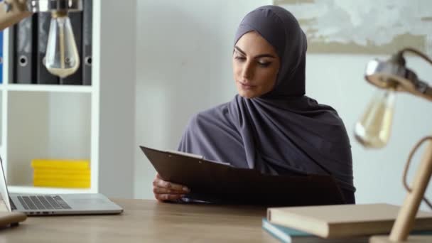 Muslim woman working with documents and throwing a thoughtful look - Felvétel, videó