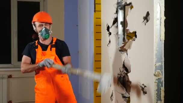 Porträt eines männlichen Arbeiters in Uniform und Atemschutzmaske mit riesigem Hammer auf der Schulter, der mit ernsten Augen in die Kamera blickt. Abrissarbeiten und Sanierungskonzept. 4 k Video - Filmmaterial, Video
