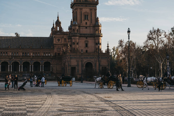 Севилья, Испания - 17 января 2020 года: Городские конные экипажи на площади Plaza de Espana, на площади Parque de Maria Luisa, в Севилье, Испания, построенные в 1928 году для иберо-американской выставки 1929 года
. - Фото, изображение