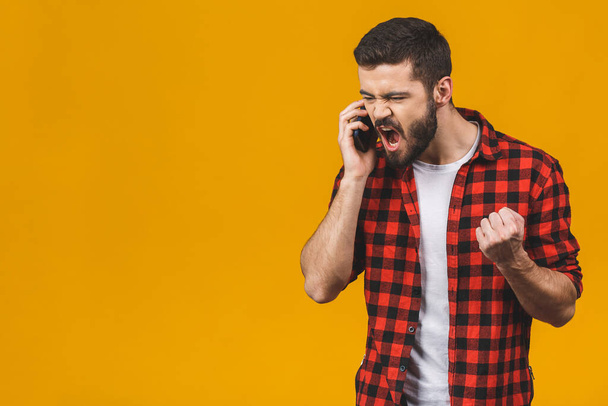 Angry young man screaming on the cell phone isolated on a yellow background.   - Zdjęcie, obraz