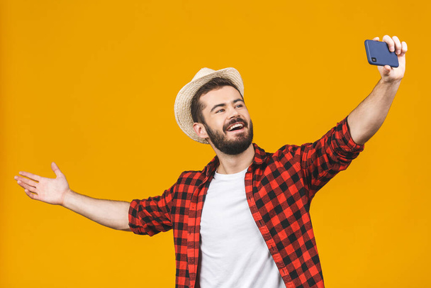 Allegro giovane uomo di viaggio in cappello scattare selfie con smartphone isolato su sfondo giallo
. - Foto, immagini