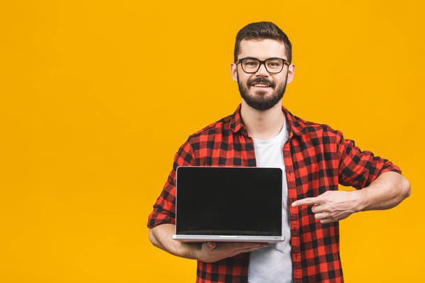 Smiling businessman pointing finger on blank laptop screen isolated over yellow background. Looking at camera. - Valokuva, kuva
