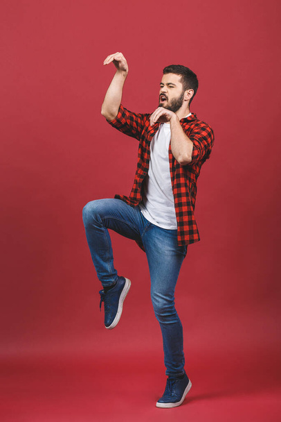 Full length portrait of an excited happy man standing on his tiptoes and with hands outstretched isolated over red background. - Fotoğraf, Görsel