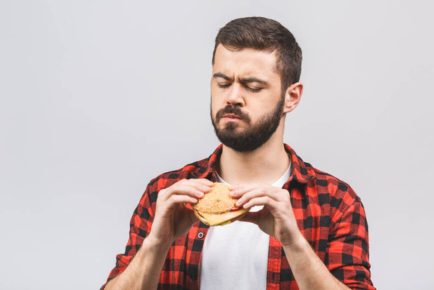 Young man holding a piece of hamburger. Student eats fast food. Burger is not helpful food. Very hungry guy. Diet concept isolated against white background.  - Photo, image