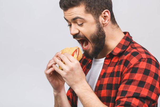 Young man holding a piece of hamburger. Student eats fast food. Burger is not helpful food. Very hungry guy. Diet concept isolated against white background.  - Fotoğraf, Görsel