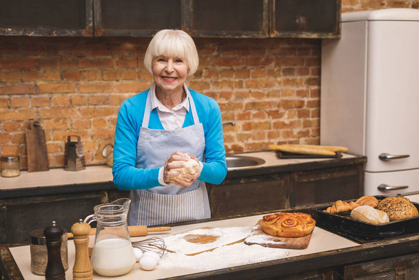 Portré vonzó mosolygós boldog idős nő főz a konyhában. Nagymama finom süteményt készít..  - Fotó, kép