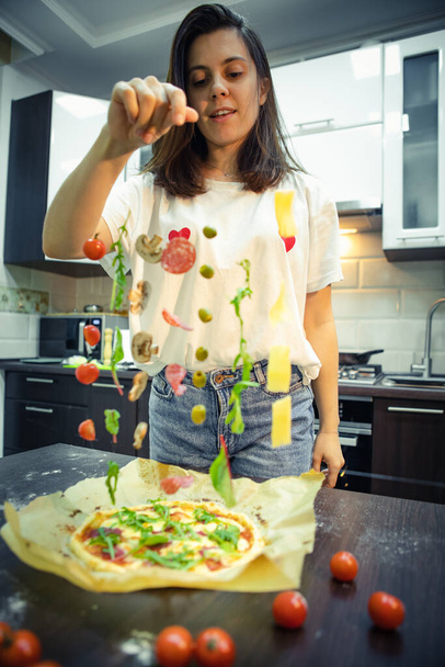 γυναίκα που φτιάχνει συστατικά πίτσας όπως μανιτάρια σαλάμι, τυρί ελιάς παγωμένο στον αέρα. σπιτικό φαγητό - Φωτογραφία, εικόνα