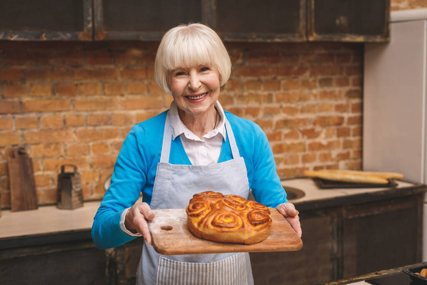 Портрет привлекательной улыбающейся счастливой пожилой женщины готовится на кухне. Бабушка делает вкусную выпечку
.  - Фото, изображение