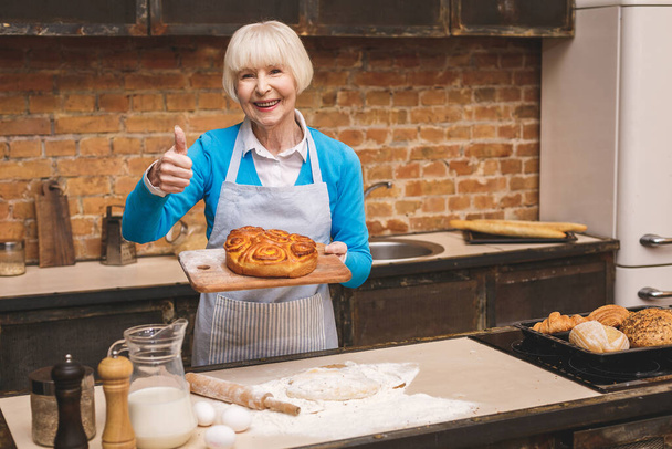 Portrait d'attrayant sourire heureuse femme âgée cuisine sur la cuisine. Grand-mère fait une délicieuse cuisson. Pouce en l'air
. - Photo, image