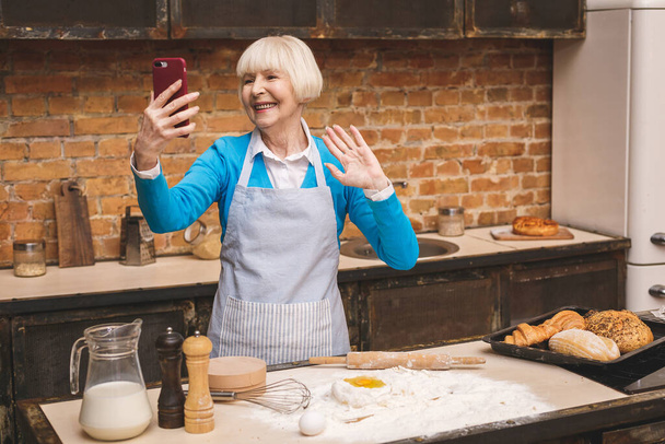 Koncepcja selfie. Portret atrakcyjnej starszej kobiety gotuje się w kuchni. Babcia robi smaczne pieczenie. - Zdjęcie, obraz