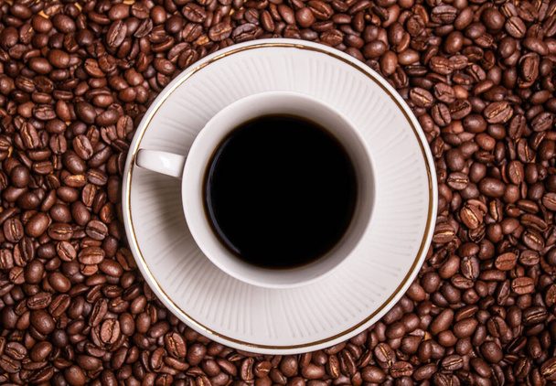 Kahve çekirdekleriyle çevrili beyaz bir fincanda sade kahve. - Fotoğraf, Görsel