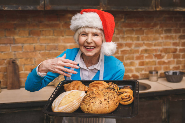 Újévi főzés. Egy vonzó idős nő portréja főz a konyhában. Nagymama finom karácsonyi sütést csinál.. - Fotó, kép
