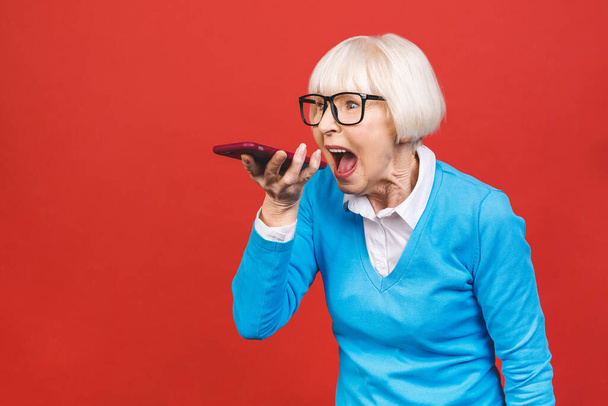 Wütende Seniorin telefoniert isoliert auf rotem Hintergrund.  - Foto, Bild
