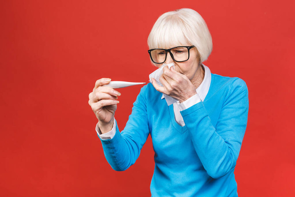 Ill allergic old mature woman blowing runny nose got hay fever rhinitis allergy flu, sick middle aged senior lady sneezing in tissue holding handkerchief isolated on red studio background. - Fotó, kép