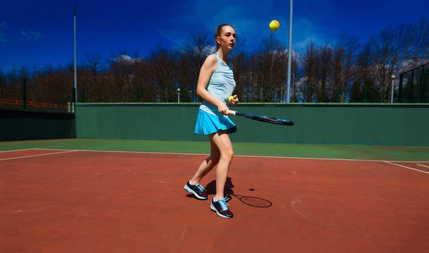 Сексуальная теннисистка в белом платье и на каблуках держит теннисную ракетку на корте. Молодая женщина играет в теннис, спорт - Фото, изображение