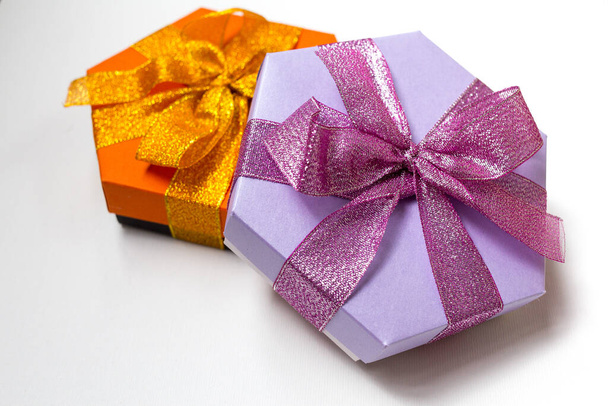 Una hermosa naranja y cajas de regalo de hexágono lila con cinta y lazo en el fondo blanco. Acostado. Lugar para el texto. Presente.
 - Foto, imagen