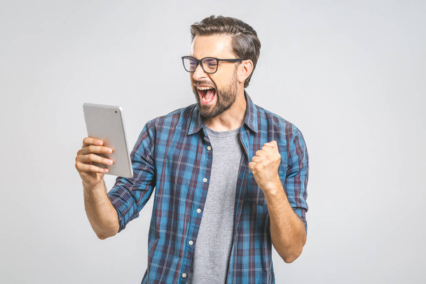 Hombre joven feliz en camisa a cuadros de pie y utilizando la tableta sobre fondo gris
 - Foto, imagen