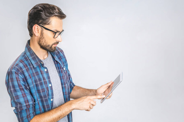 Idee! Denkender junger Mann im karierten Hemd im Stehen und Tablet vor grauem Hintergrund. - Foto, Bild