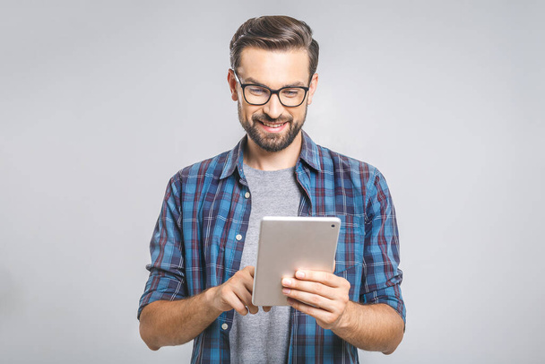Glücklicher junger Mann im karierten Hemd, der vor grauem Hintergrund steht und Tabletten benutzt - Foto, Bild